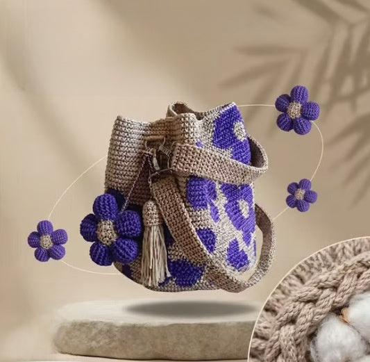 Purple floral crochet cotton bucket bag with detachable flowers and a tassel on a pedestal