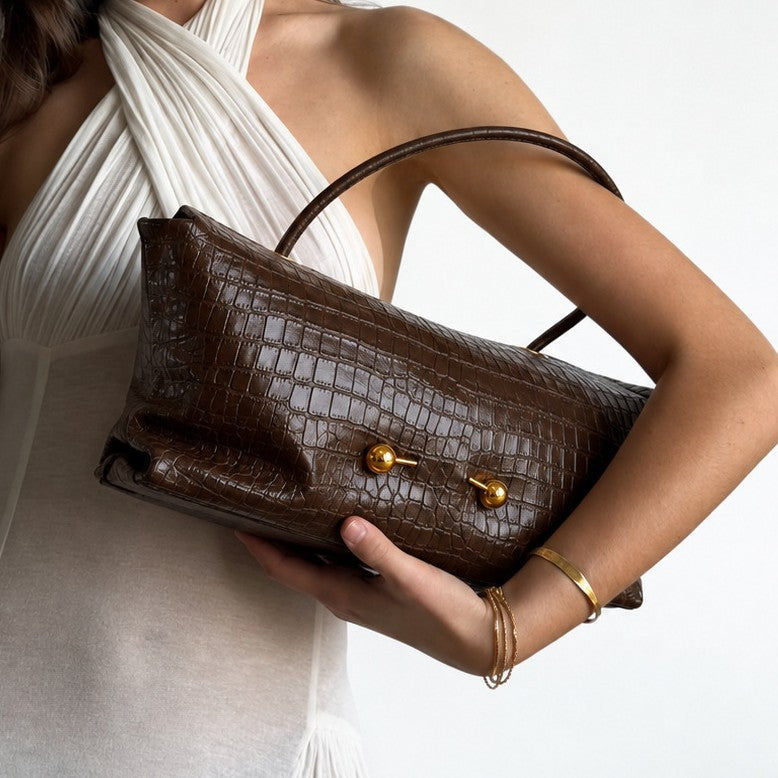 Woman in a white halter top carrying a dark brown croc embossed shoulder bag under her arm