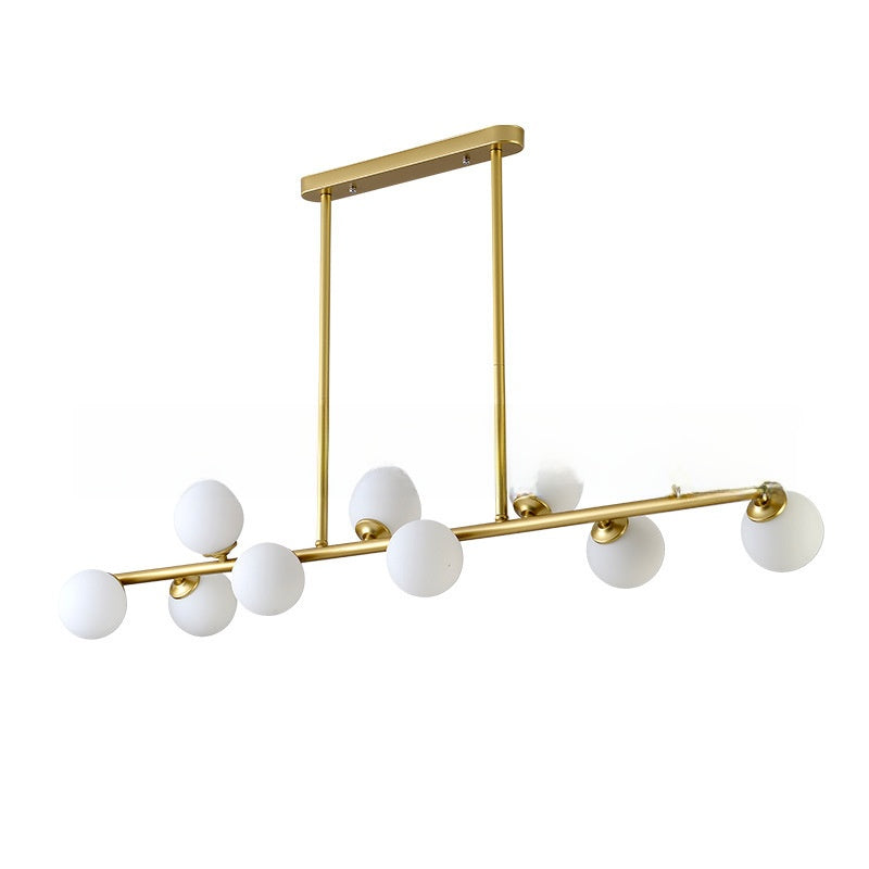 Gold linear pendant light with six milky white glass globe shades at staggered heights on a white background