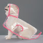 Small white dog seated in a clear EVA hooded rain poncho with sakura pink trim, studio three quarter view