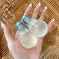 Two milky bulb squeeze toys with moulded grey screw bases resting in a hand over rattan