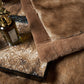 Close-up of the camel fur pile and the smooth brown border at the corner of the blanket, with a perfume bottle