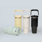 Insulated tumblers with handles in yellow, cream and black, with a sage green tumbler lying on its side