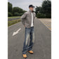 Man in a gray cotton jacket and jeans standing on a paved road, hands in the pockets