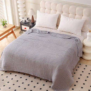 Crinkled multi layer cotton gauze blanket folded across the foot of a made bed
