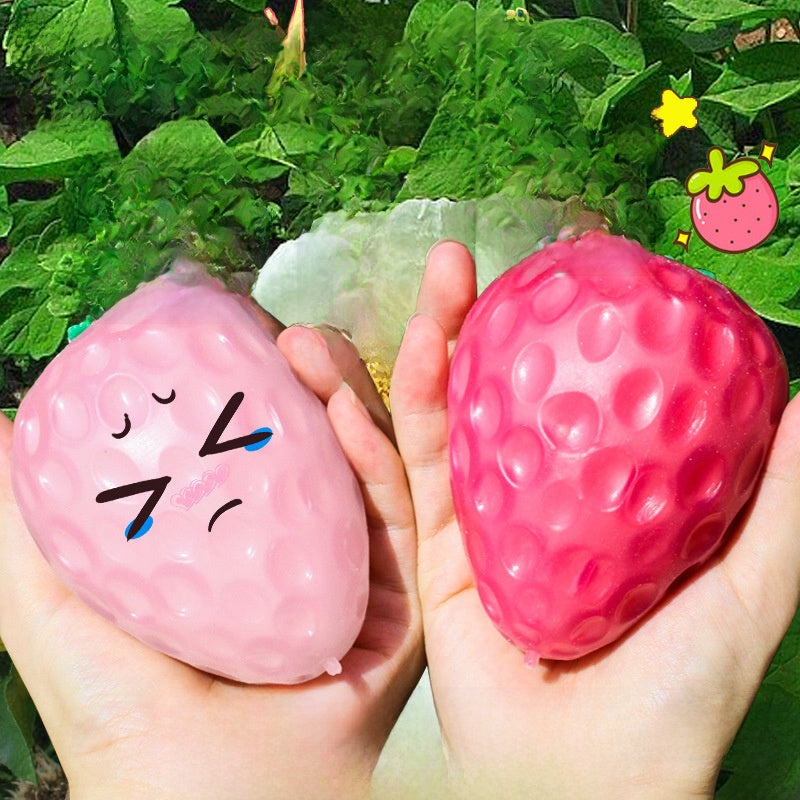 Two dimpled strawberry squeeze toys in two hands, one pale rose and one deep pink