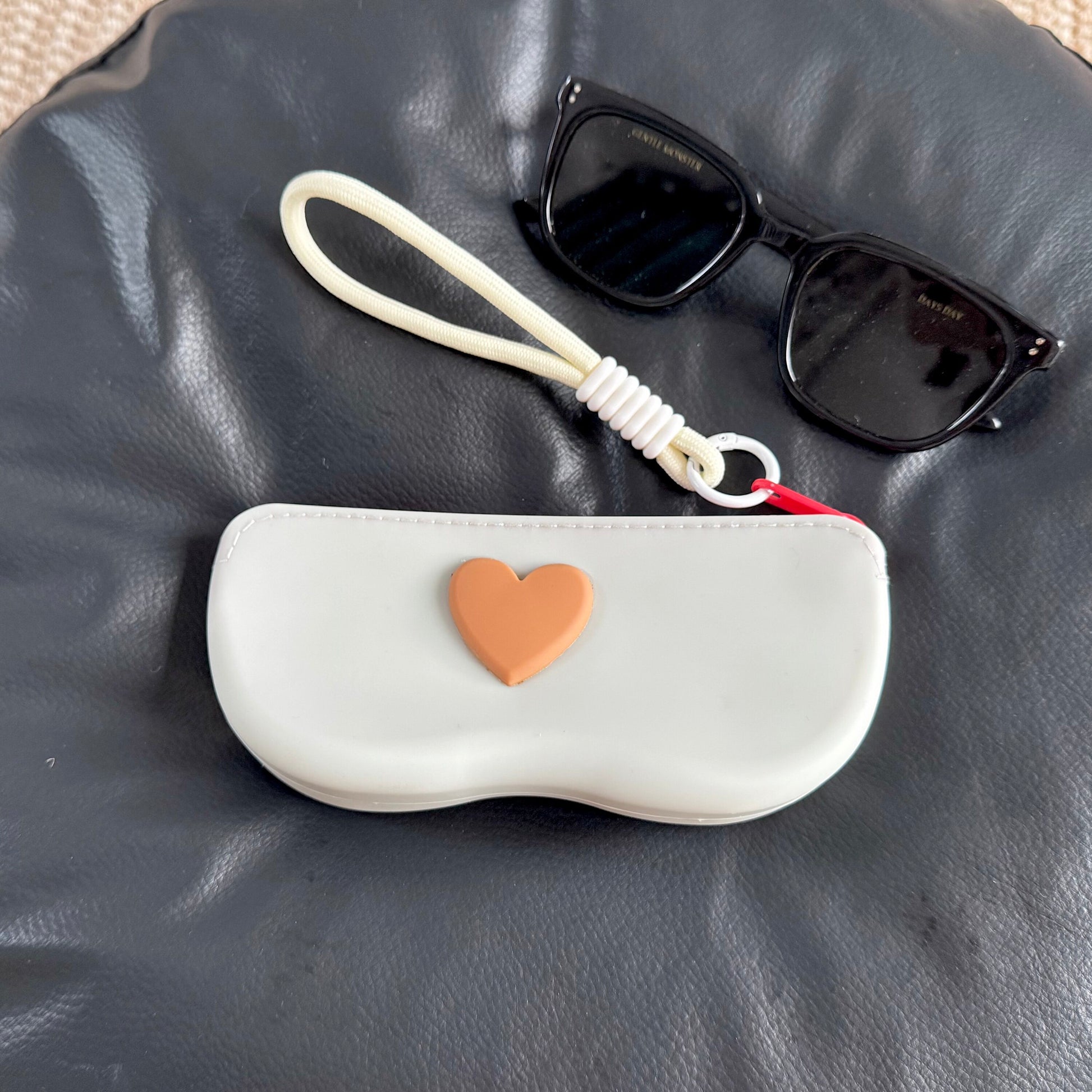 Four pastel silicone sunglasses cases with raised hearts and braided wrist lanyards on a clip