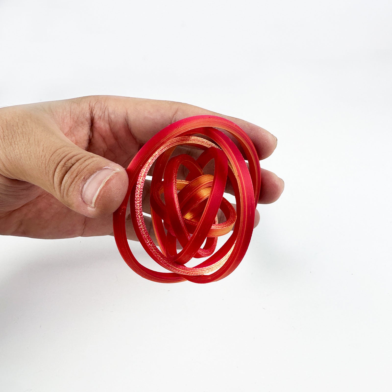 Red and gold gyro ring fidget opened into a hollow sphere between finger and thumb