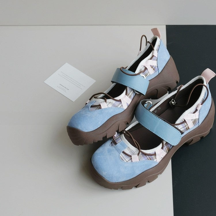 Pair of sky blue platform shoes with a wide strap, patterned panels and a brown lug sole on a grey and black surface