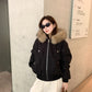 Woman in a black hooded bomber jacket with vegan fur trim and silver zip, wearing sunglasses and cream trousers