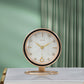 White shell pattern dial desk clock with black bezel on a round gold tone ring base, in front of a green curtain
