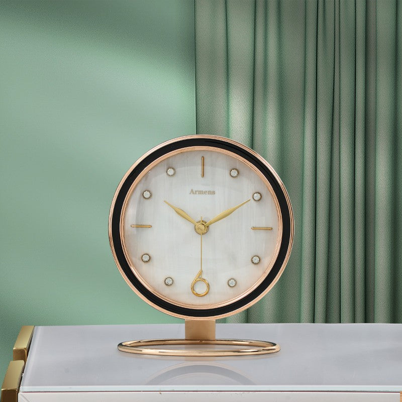 White shell pattern dial desk clock with black bezel on a round gold tone ring base, in front of a green curtain