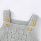 Pink knitted baby romper laid flat beside small baby shoes, square neck and straps