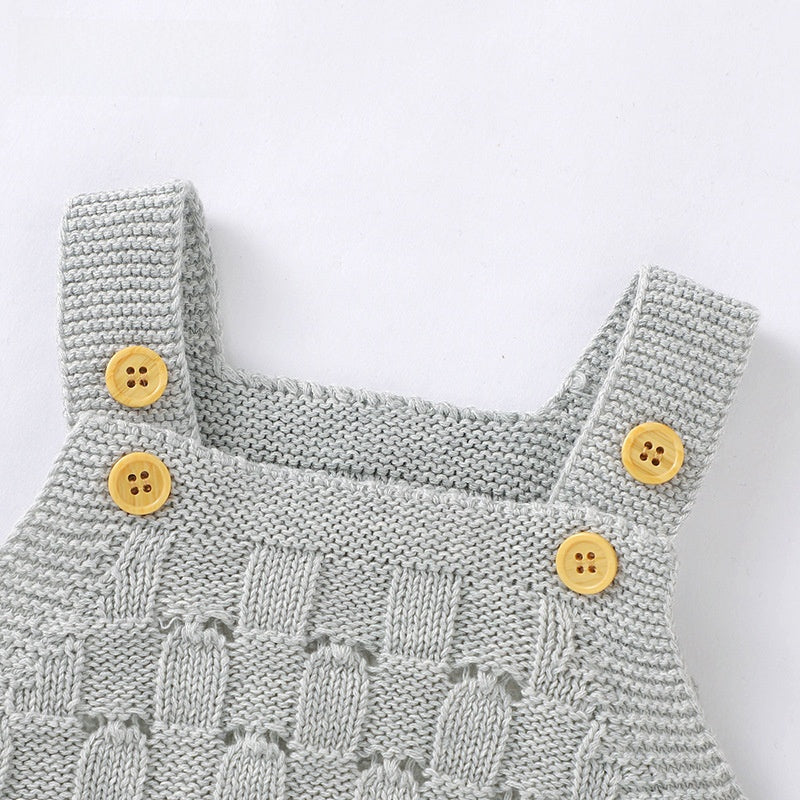 Pink knitted baby romper laid flat beside small baby shoes, square neck and straps
