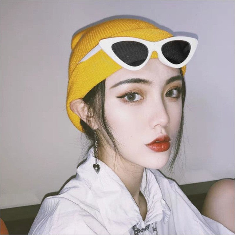 Woman in a yellow beanie wearing white framed cat eye sunglasses perched on her face