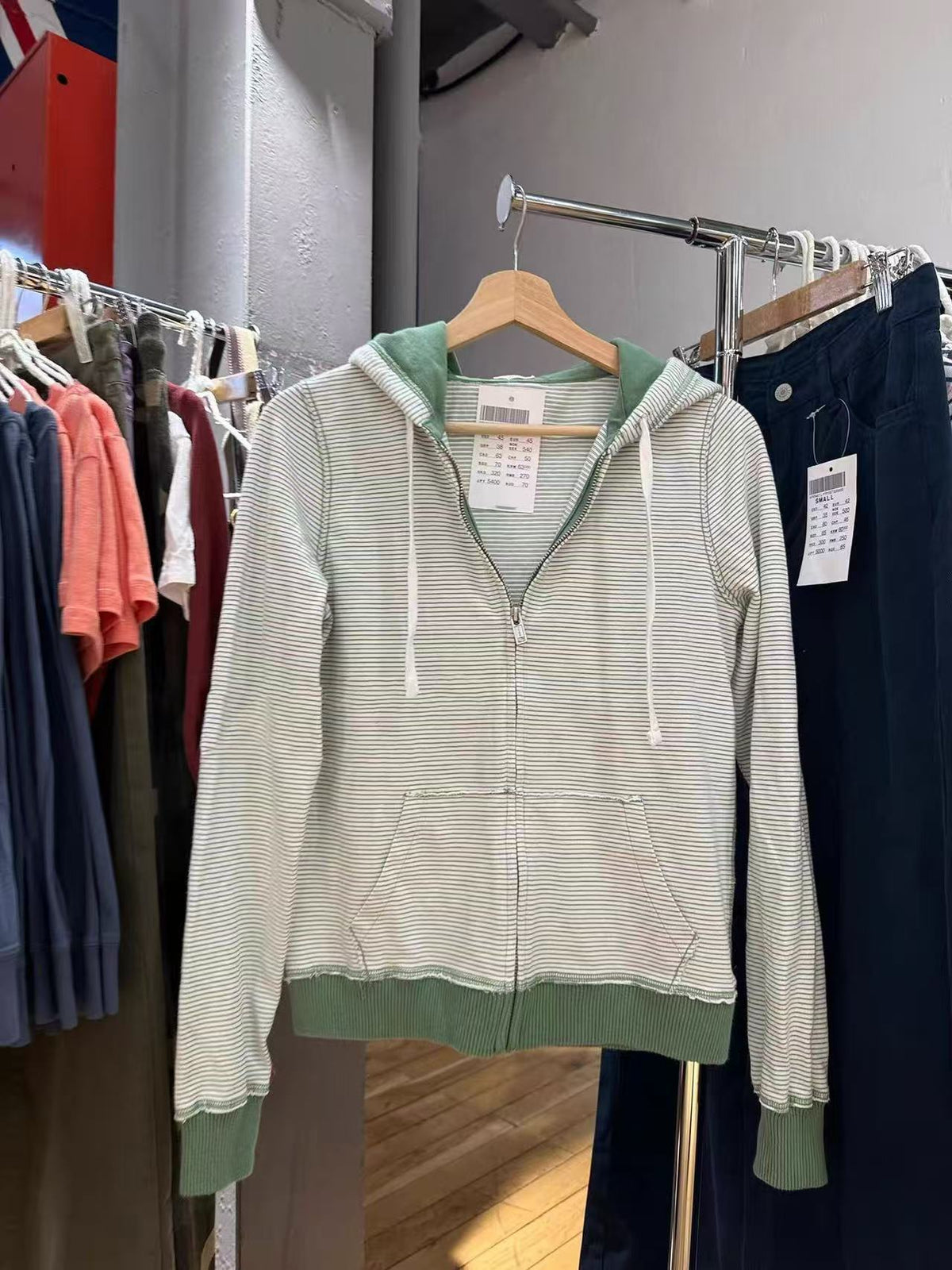 Green striped zip-up hoodie on a hanger at a clothing rack with a hang tag