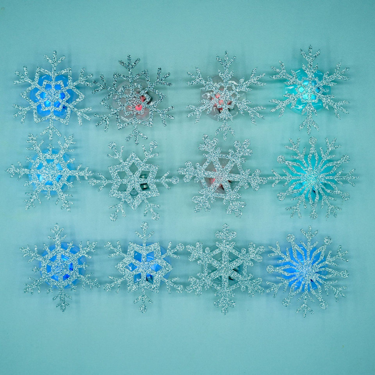 A set of silver glitter snowflake stickers on a teal background with blue and red lit centers