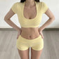 Studio front view of a pale yellow U-neck crop top and fold-over shorts with hands on hips
