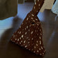 Brown triangle pouch bag with cream spots and a looped handle on a wooden table, option Brown Spots
