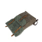 Olive green and teal green canvas backpack laid flat showing the buckled front flap and brown straps