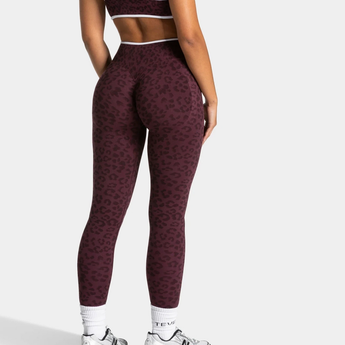 Back view of burgundy seamless leopard print leggings with a matching bra and white contrast edges worn with white socks