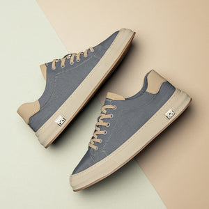 Grey canvas low top sneakers, sand laces and cream flat sole, paired on a two tone studio backdrop