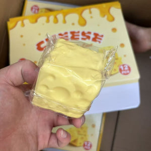 Wrapped cheese cube squishy held in a hand in front of the printed cheese counter box