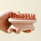 Cream and rust silicone scalp shampoo brush held in a hand showing the bristles