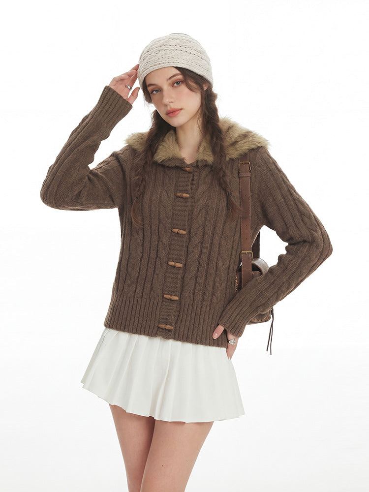 Woman wearing the coffee brown cable knit cardigan with wooden toggles and fur trimmed hood, hand raised to a beanie