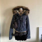Navy blue short hooded jacket with a fur trimmed hood on a mannequin with a cross necklace, belt and bag