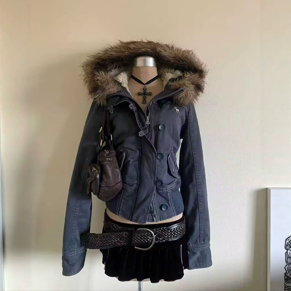 Navy blue short hooded jacket with a fur trimmed hood on a mannequin with a cross necklace, belt and bag