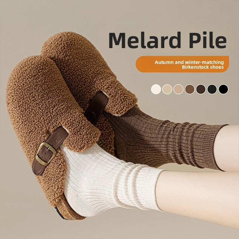 Brown and cream ribbed socks worn with a shearling clog on a beige background with a row of color dots