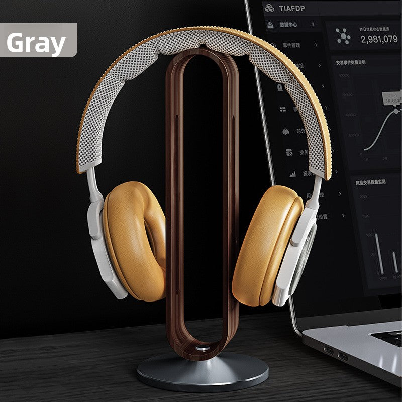 Gray walnut headphone stand holding over ear headphones beside a laptop on a dark desk