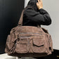 Large brown multi-pocket shoulder bag worn on the shoulder with zip pockets on the front and both ends