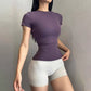 Woman in a dark purple fitted short sleeve fitness T-shirt with light gray shorts, three-quarter studio view