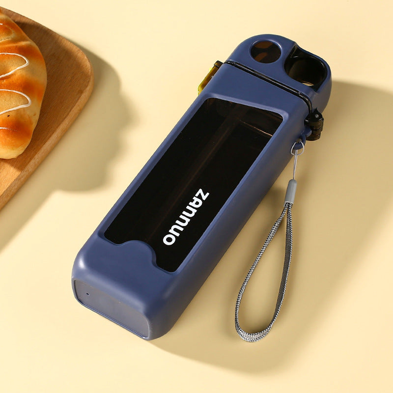 Navy square plastic sports water bottle lying flat with grey woven carrying strap beside bread