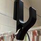 Close up of a black resin hook with a round hole on a glass door edge, a small metal hook through the hole