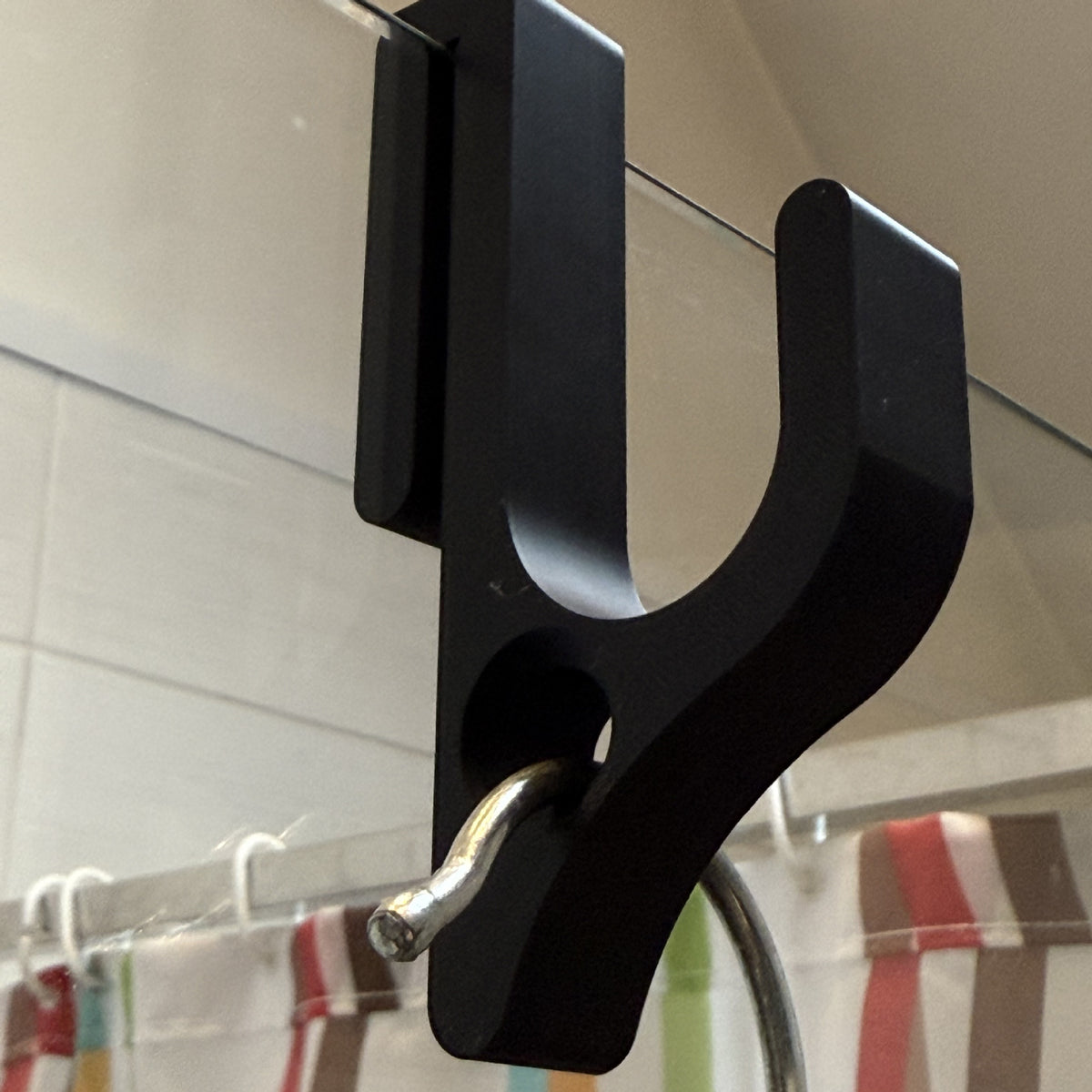 Close up of a black resin hook with a round hole on a glass door edge, a small metal hook through the hole