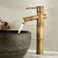 Tall antique copper bamboo basin faucet pouring water into a dark grey stone vessel bowl