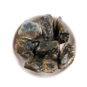 Top view of raw moonstone stones in a white dish showing grey bodies and blue flash