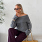 Grey off-shoulder fold-over knit sweater with wide cuffs worn with burgundy trousers
