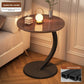 Dark walnut tone round top side table with a black steel C frame and disc base beside a bed, option Dark Walnut