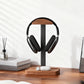 Wooden headphone stand with storage tray base for earbuds beside books on a wood desk