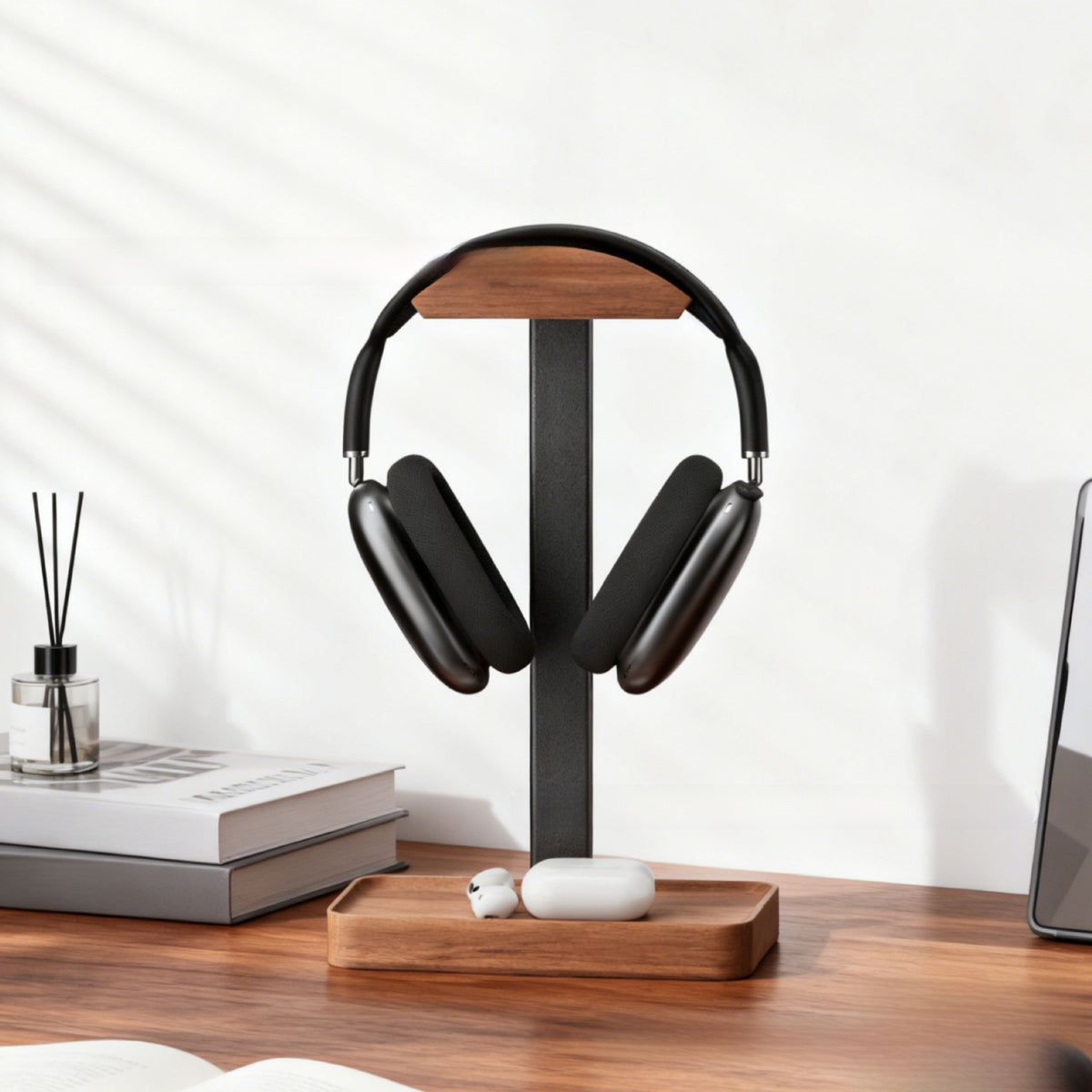 Wooden headphone stand with storage tray base for earbuds beside books on a wood desk