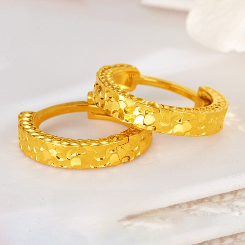 Pair of gold-plated hoop earrings with a crushed ice textured face and a ridged edge on a white marble surface