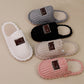 Four ribbed plush slippers in white, black, khaki and pink on a beige surface, each with a brown Original label