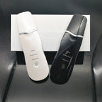 White and black ultrasonic facial skin scrubbers resting on a white retail box with steel spatula heads