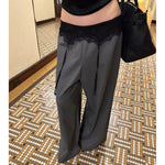 Gray wide-leg pants worn with black lace waist panel and handbag in hallway