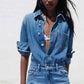 Close view of denim jumpsuit collar, metal buttons, chest patch pocket and waistband button on a model