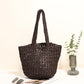Coffee paper straw shoulder bag standing upright beside a glass vase of eucalyptus